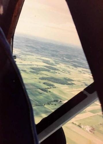 Sit in the doorway (with legs outside) look straight down to spot landing zone and give pilot heading for jump run